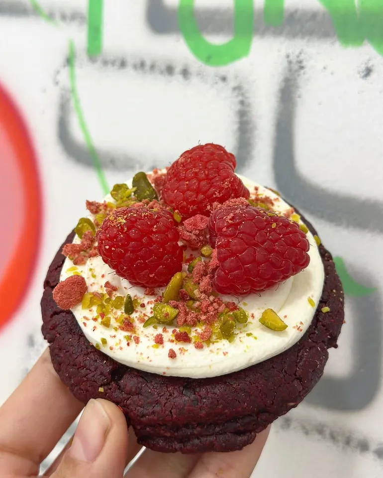 Cookie red velvet con frosting, frambuesas y pistacho